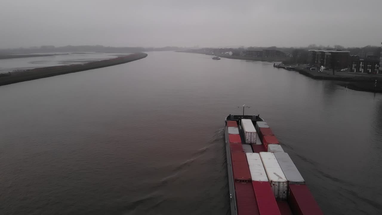 Container sized cargo vessel navigating on a dutch river heading to the port of Rotterdam on a windless misty day. Drone dolly slowmo shot