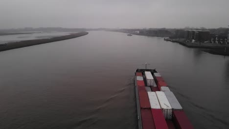 container sized cargo vessel navigating on a dutch river heading to the port of rotterdam on a windless misty day. drone dolly slowmo shot