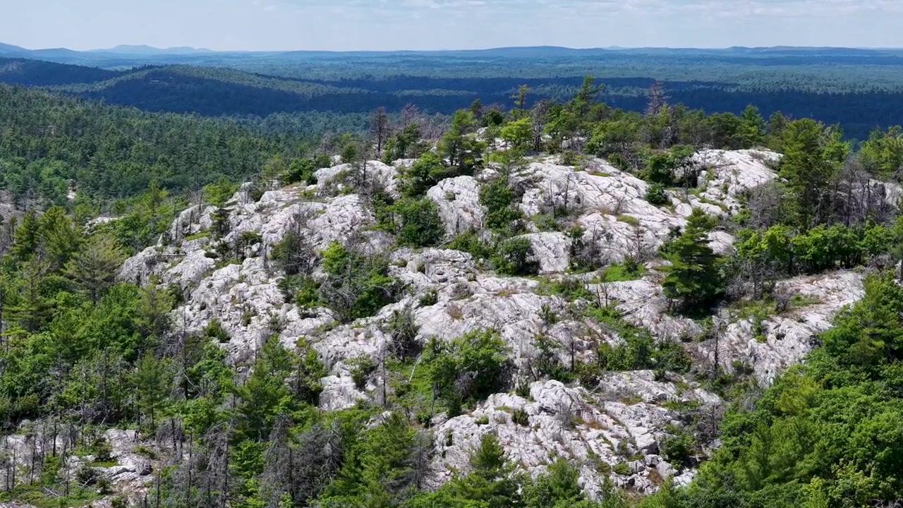 Drone svæver over lyse granitfremspring og vindblæste træer langs en barsk vildmarksryg i det nordlige Ontario, Canada