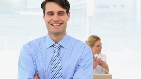 Businessman-smiling-at-camera-with-colleague-behind-him