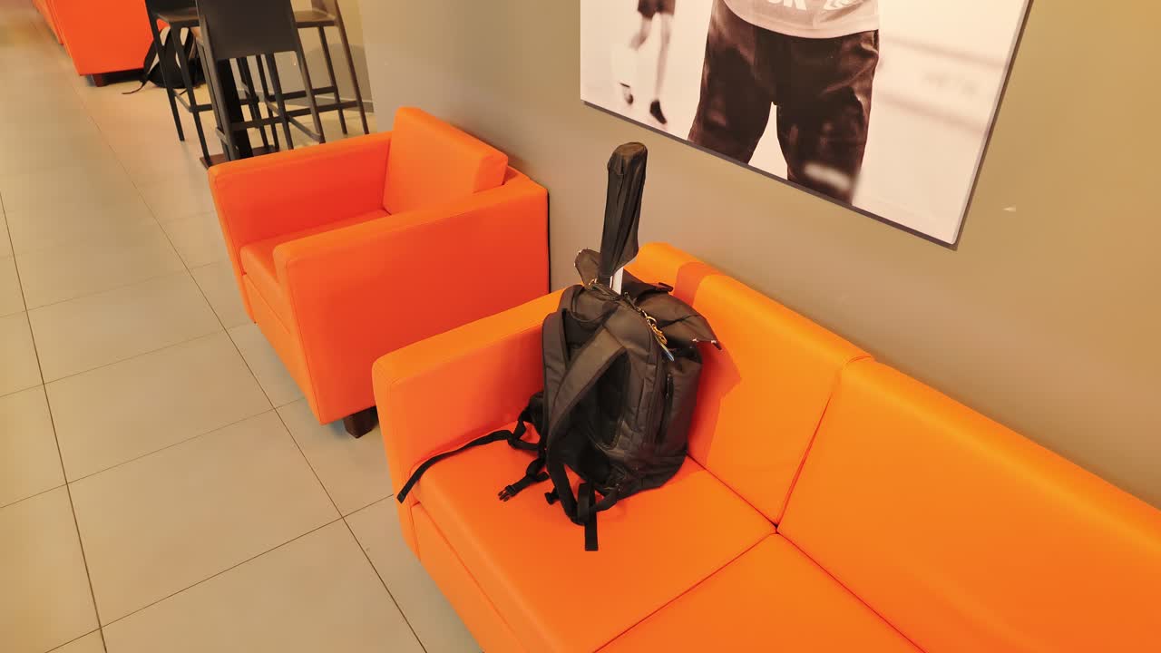Young man picks up squash bag with racket from bright orange sofa in hallway