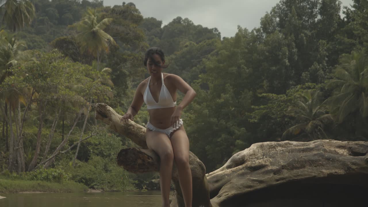 una chica sexy sentada en un tronco de árbol caído antes de ser mordida por un insecto y salta del tronco