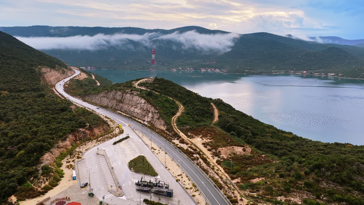 Hırvatistan, Pelješac Köprüsü çevresindeki doğal kıyı bölgesinin havadan drone görüntüsü; kıvrımlı yollar, yoğun yeşil tepeler, sudaki istiridye çiftlikleri ve dağların üzerinde yuvarlanan sis