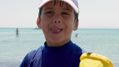 Close-up-on-face-of-caucasian-kid-smiling-at-camera,-with-sea-in-the-blurry-background,-slow-motion-120fps