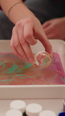 madre y niña pequeña rodan huevos en una bandeja con pinturas y agua aceitosa en la mesa closeup cámara lenta. arte turco ebru para decoración de vacaciones de pascua y feria