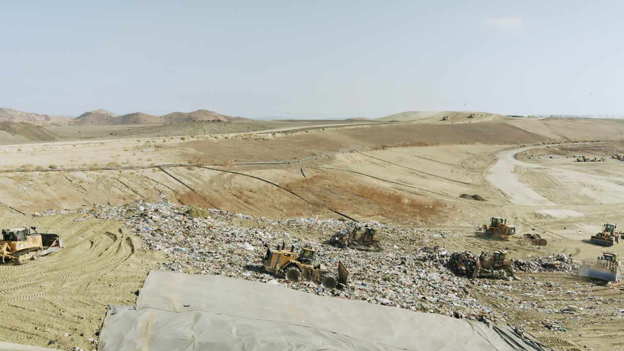 Panoramic view of a large landfill with heavy machinery compacting garbage
