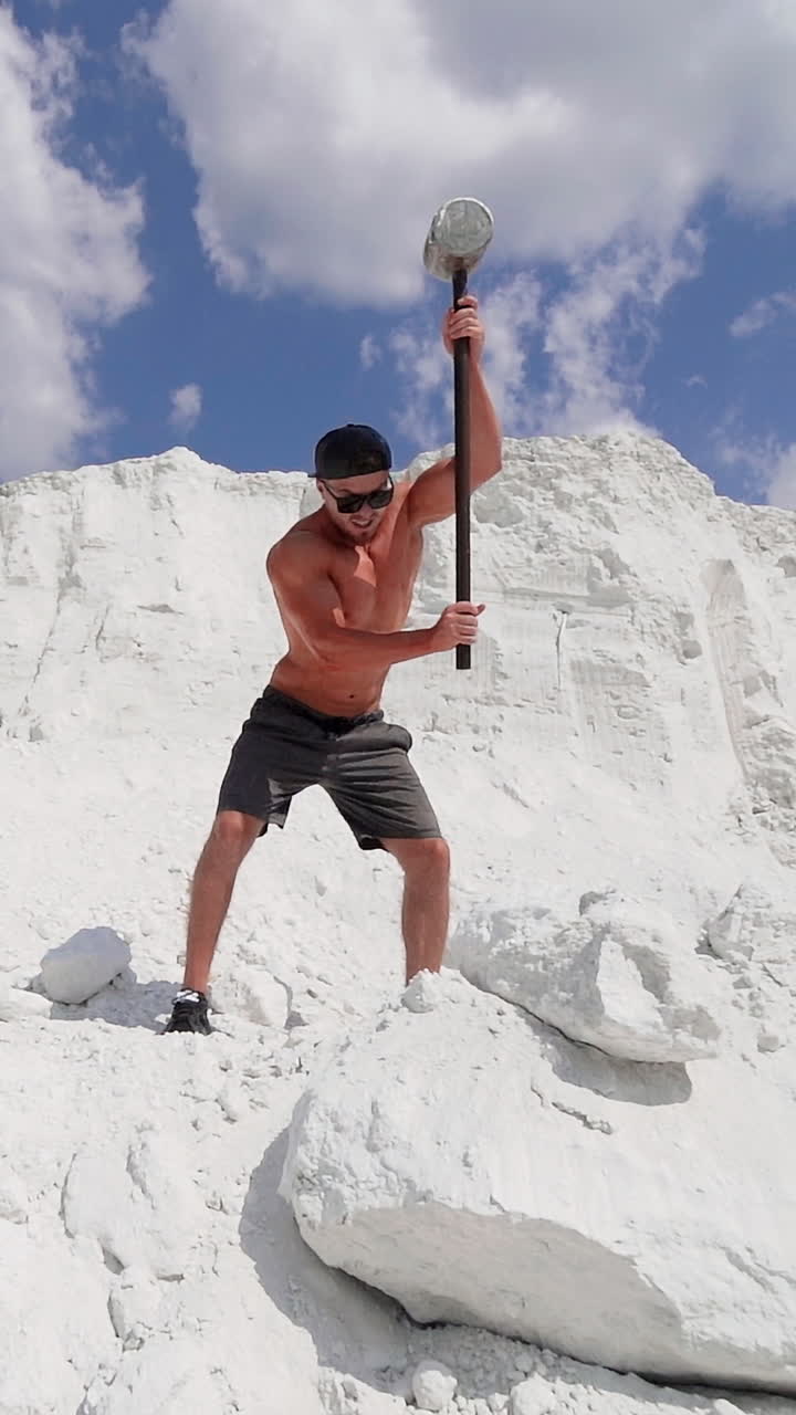 Sportsman with hammer on the hill. Shirtless athlete training with hammer on white mountain in summer. Handsome man with muscular body outdoors. Vertical video