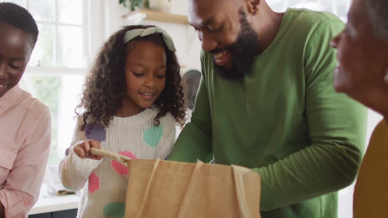 Video of happy african american parents with daughter and grandmother unpacking food shopping