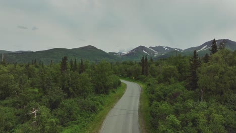 Camino-De-Campo-Con-Vegetación-Exuberante-Y-Montañas-En-El-Fondo-En-Alaska---Toma-Aérea-De-Drones