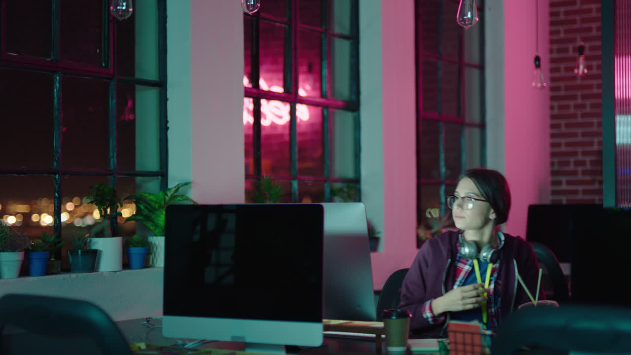 young caucasian business woman student working late using computer typing research project browsing online brainstorming deadline in trendy office at night wearing headphones