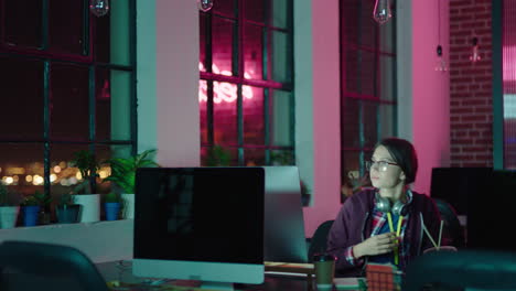 young caucasian business woman student working late using computer typing research project browsing online brainstorming deadline in trendy office at night wearing headphones