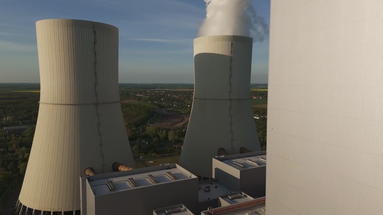 Low-altitude drone flyby past the massive cooling towers of Lippendorf coal power plant near Leipzig, Germany. Industry meets rural landscape in evening light.