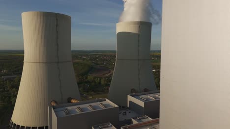 low-altitude drone flyby past the massive cooling towers of lippendorf coal power plant near leipzig, germany. industry meets rural landscape in evening light.