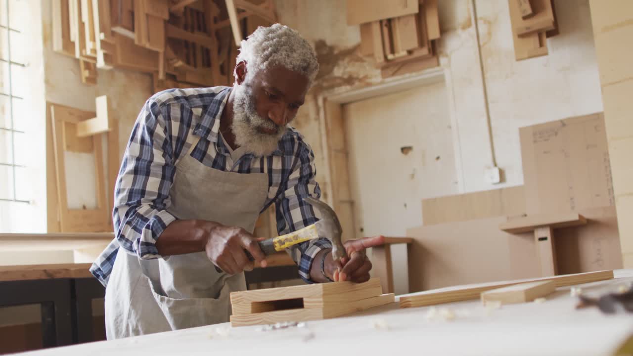 African american male carpenter hammering nails into the wood at a carpentry shop