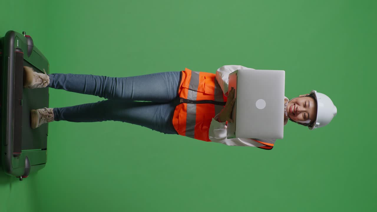 cuerpo lleno de ingeniera femenina asiática con casco de seguridad trabajando en una computadora portátil mientras camina en el estudio de fondo de pantalla verde