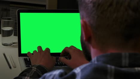 hombre escribiendo en el teclado del portátil con la tecla de croma de pantalla verde mientras está sentado en la oficina de casa. joven utiliza la computadora para el trabajo remoto, la educación en línea o la comunicación en casa. cerca. cámara lenta