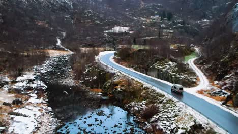 car driving on a winding road through a snowy mountain landscape in norway, aerial view