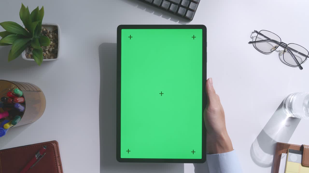 vista de arriba hacia abajo de una computadora portátil con pantalla verde simulada pantalla chromakey en un escritorio de oficina de madera al lado de la libreta con bolígrafos, gafas y un vaso de agua.