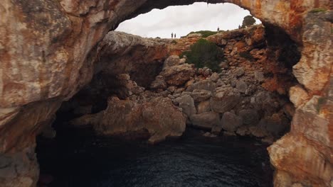 tourists standing on a cliff - flying through a cave with a drone at the beautiful coastline in mallorca, spain - 4k