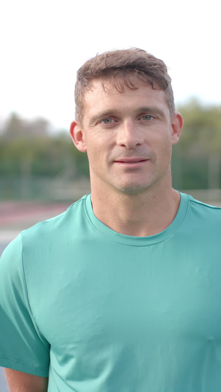 Vertical video of portrait of happy caucasian man at tennis court in slow motion