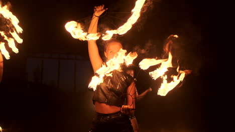 Three-women-with-burning-hoops-dance-with-fiery-torches-in-leather-clothes-in-a-dark-hangar-demonstrating-a-circus-fire-show-in-slow-motion