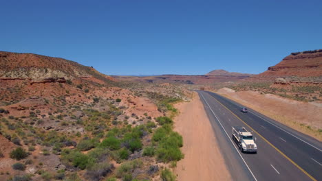 ascending drone shot starting from ground level to 200 feet up of a car and truck driving down a road running through mount zion with mountain range in the background located in southern utah