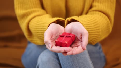 una mujer sentada en un sofá presentó un pequeño regalo en las palmas de sus manos - cerca