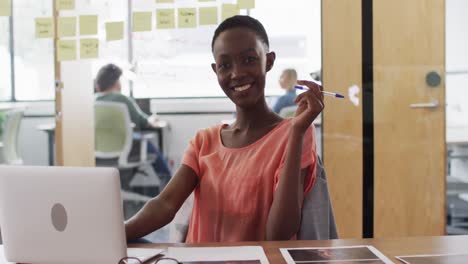 Porträt-Einer-Afroamerikanischen-Geschäftsfrau,-Die-Mit-Laptop-Am-Schreibtisch-Sitzt-Und-Im-Büro-Lächelt