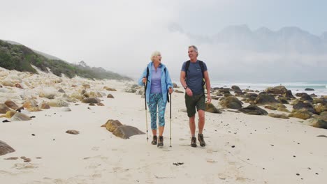 senior hiker couple with backpack and hiking poles talking to each other and walking while hiking