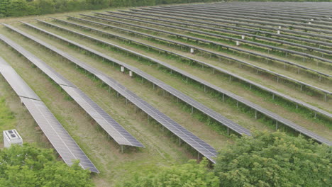 aerial fly by of a large solar panel farm amongst green english fields and trees in the countryside