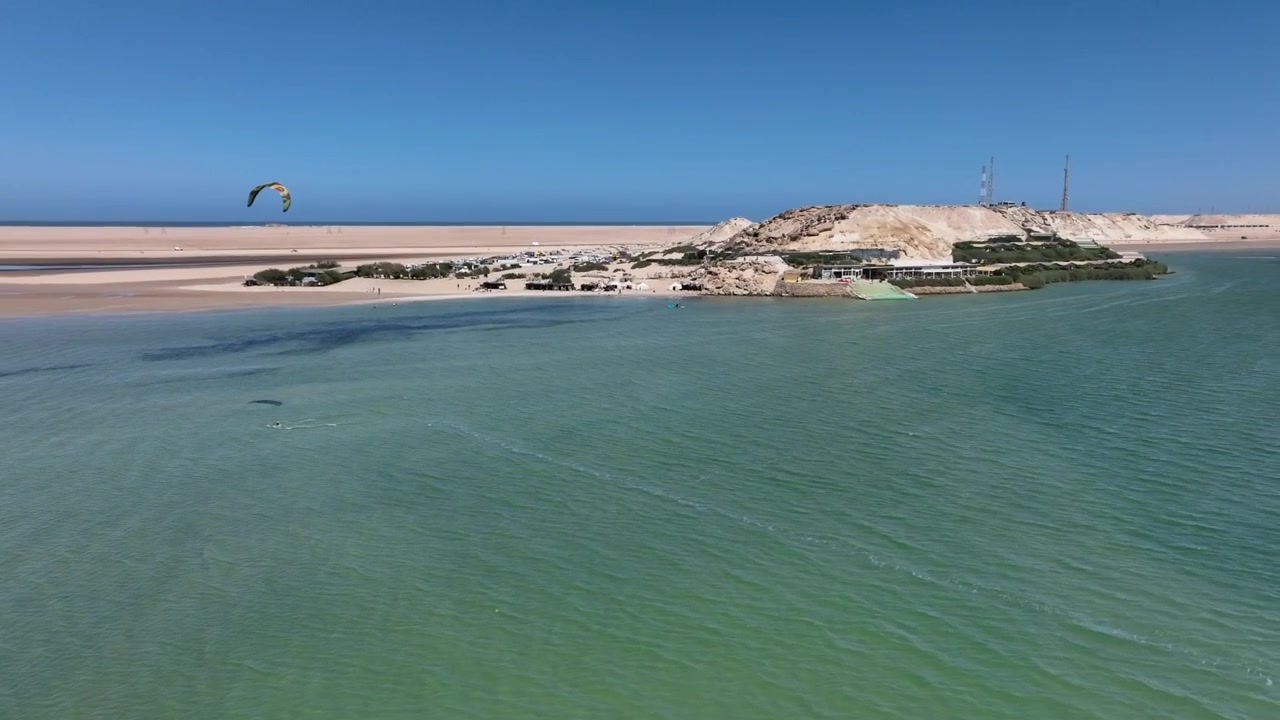 Drone luftfoto af en kitesurfer, der navigerer i Dakhla-bugtens beskyttede farvande med ørkenkystlinjer og kystlandskaber i det sydlige Marokko. Ikonisk destination for vindsport og eventyrturisme