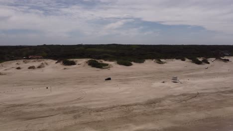 Luftaufnahme-Eines-4x4-Fahrzeugs,-Das-Bei-Sonnenlicht-Am-Sandstrand-Von-Mar-De-Las-Pampas-Fährt---Meereswellen,-Die-Die-Küstenlinie-Erreichen