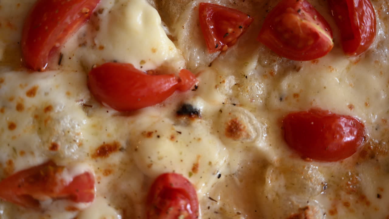 Primo piano di pizza appena sfornata, guarnita con formaggio fuso e pomodorini