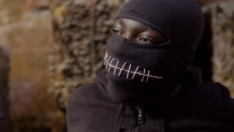 close up view of man wearing black balaclava and holding an ax in a ruined building