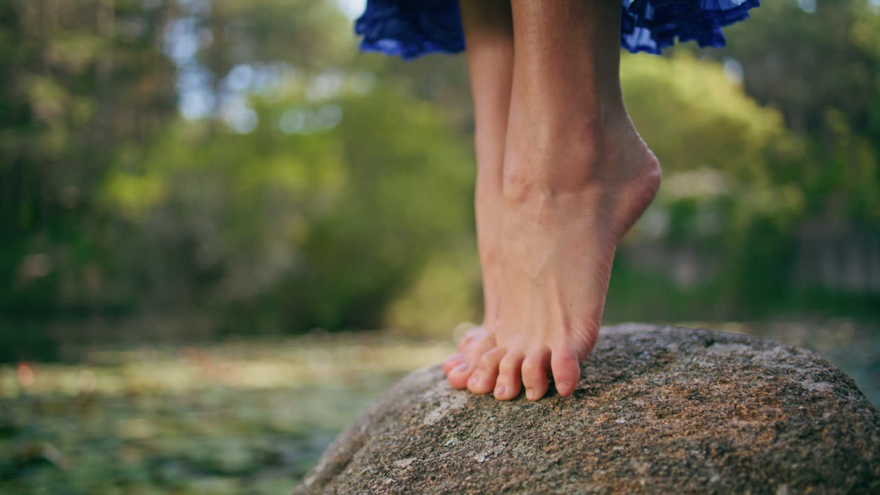 Girl feet stand tiptoes on stone at forest landscape close up. Beautiful legs