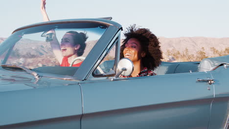excited female friends driving convertible car on a highway