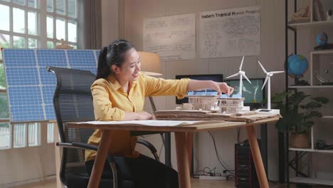 side view of asian woman positively shaking her head while building model of a small house with solar panel