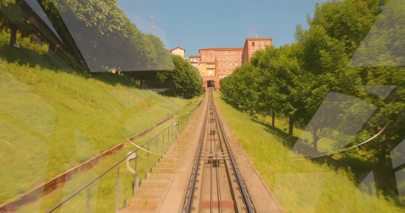 Kaunis POV-ajelu historiallisella funikulaarilla Mondovissa, Italiassa. Katsaus alas raiteita pitkin auton sisältä sen noustessa vihreää rinnettä ylös kohti vanhaakaupunkia.