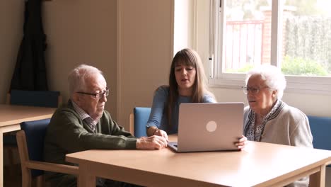 happy granddaughter teaching senior man and woman to use laptop at nursing home