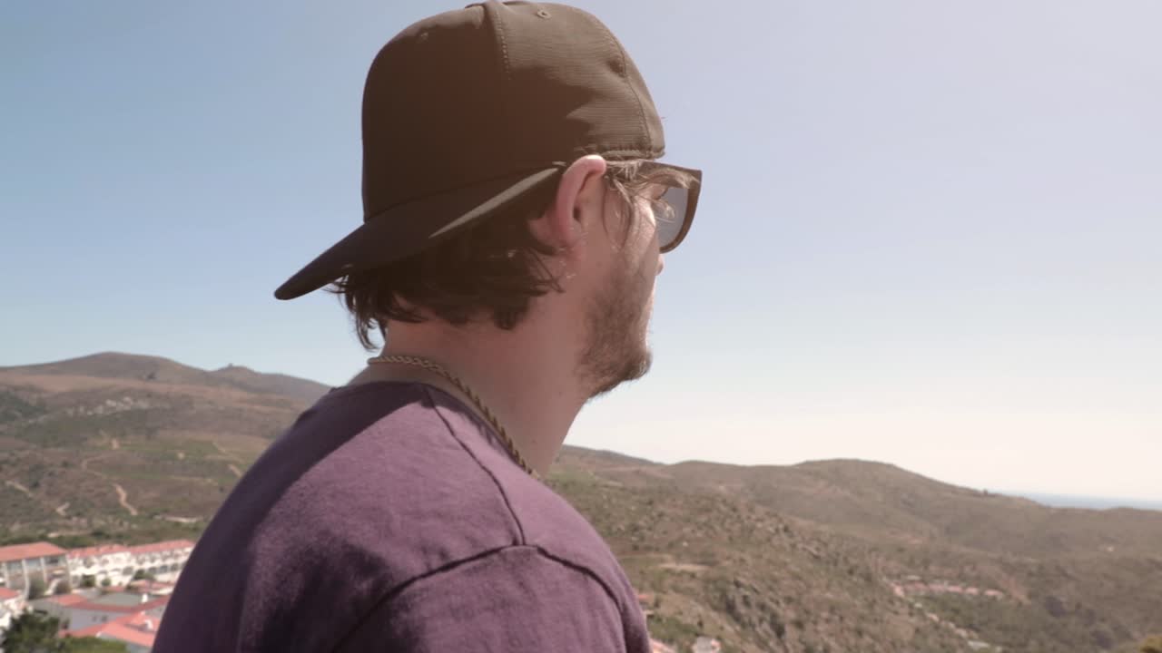 화창한 여름날 언덕 주위를 걷는 야구 모자와 선글라스를 쓴 남자