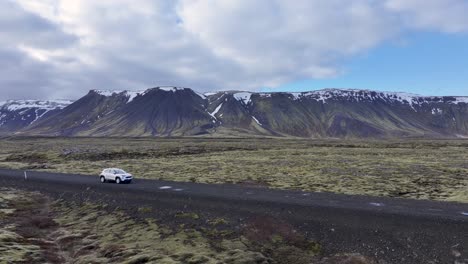 drone footage showcases an abandoned iceland farm, nestled in a rugged landscape, with a silver suv, ruined structures, and silos with colorful graffiti.