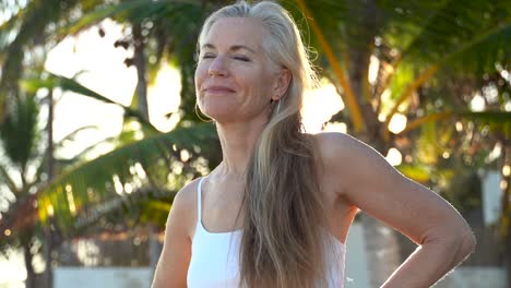 smiling woman looks off camera and then nods in agreement and then looks off camera again with sun and palm tree behind her