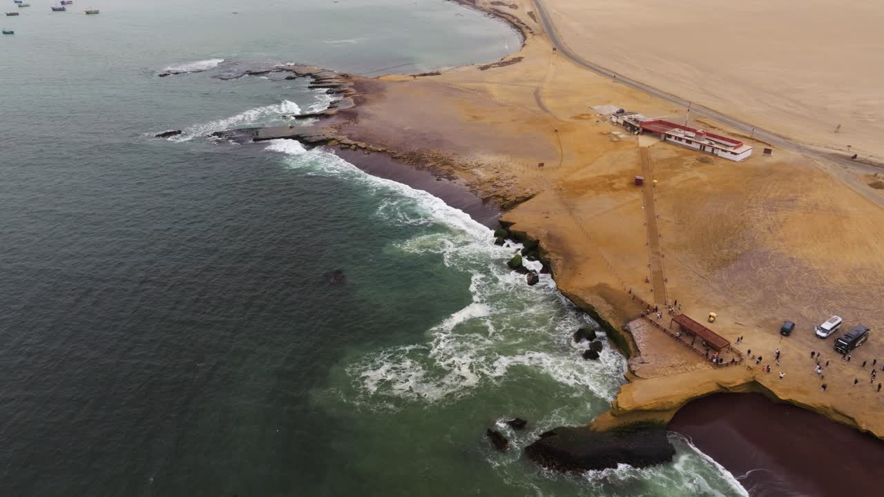 Aerial orbit over tour groups exploring rugged coastline with steep escarpments and strong surf along Paracas bay