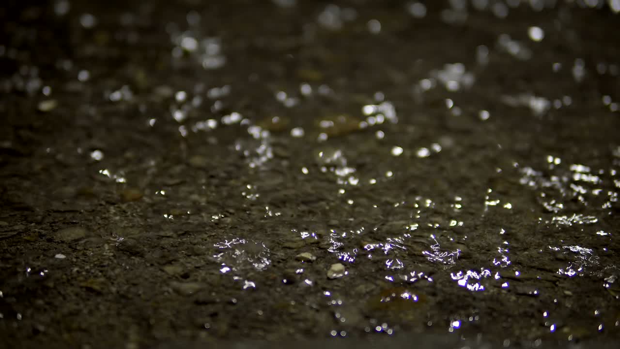 Rain falling splashes down on asphalt flooded pavement. Loopable background