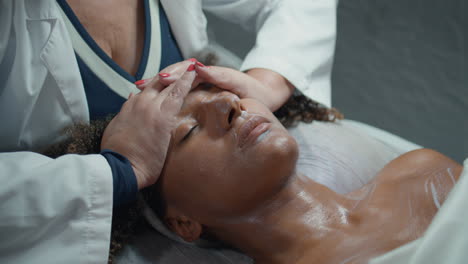 cosmetologist hands rubbing face cream on moisturizing spa procedure closeup