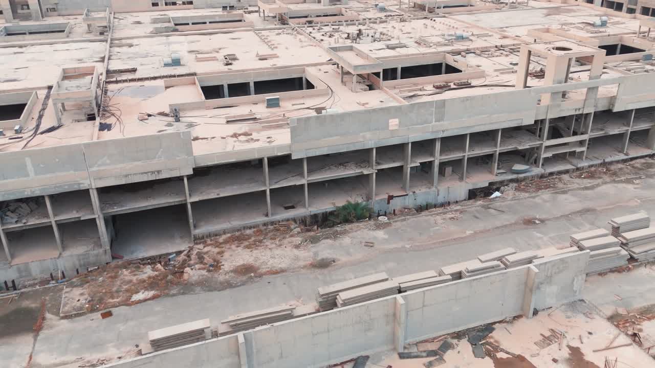 Aerial drone view of a halted construction project featuring stacks of unused concrete slabs and pavers left decaying next to an unfinished multi-story building skeleton