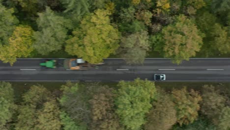 coming in aerial shot of a car which is driving fast over a autumn colored street in a forest with oncoming traffic of a tractor