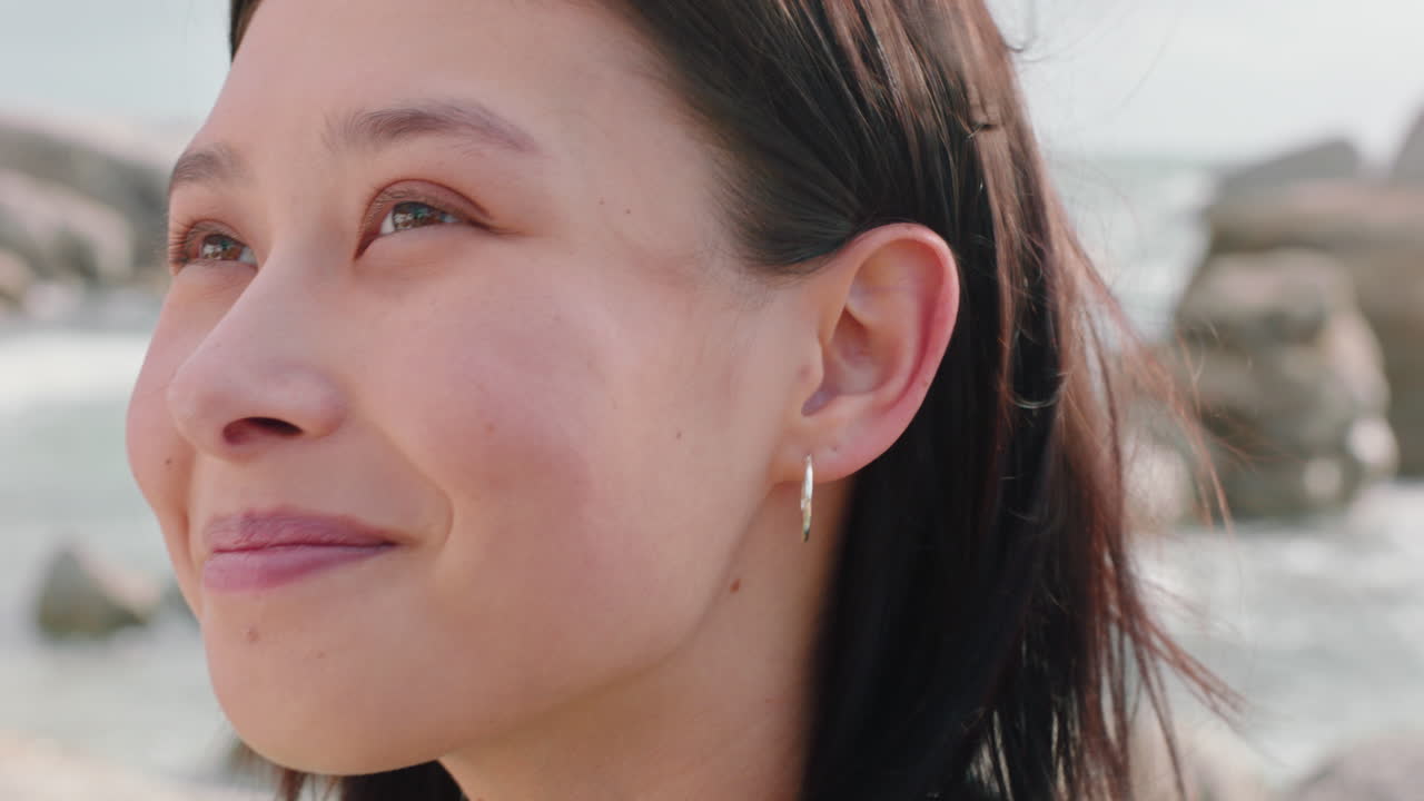 retrato de una hermosa mujer asiática sonriendo disfrutando de la playa nublada explorando el estilo de vida de vacaciones con el viento soplando el cabello en la playa