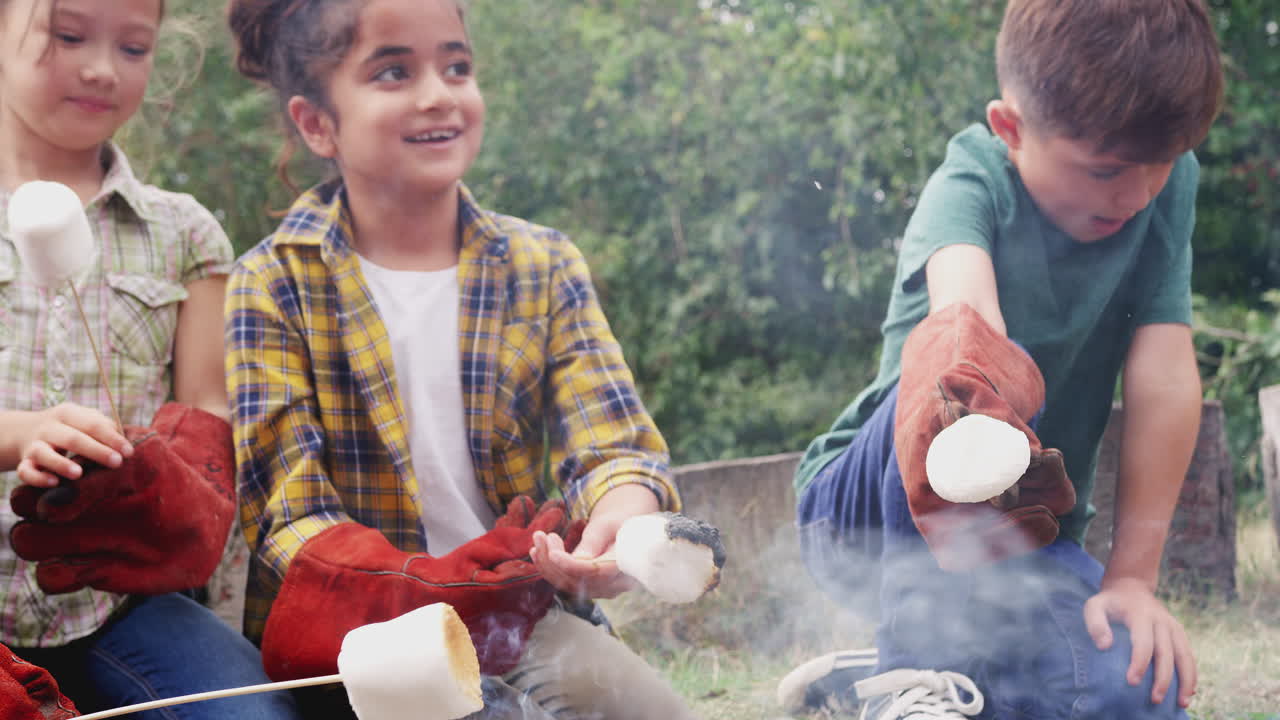 Gruppo di bambini in gita in campeggio all'aperto che arrostiscono marshmallow su un fuoco da campo insieme