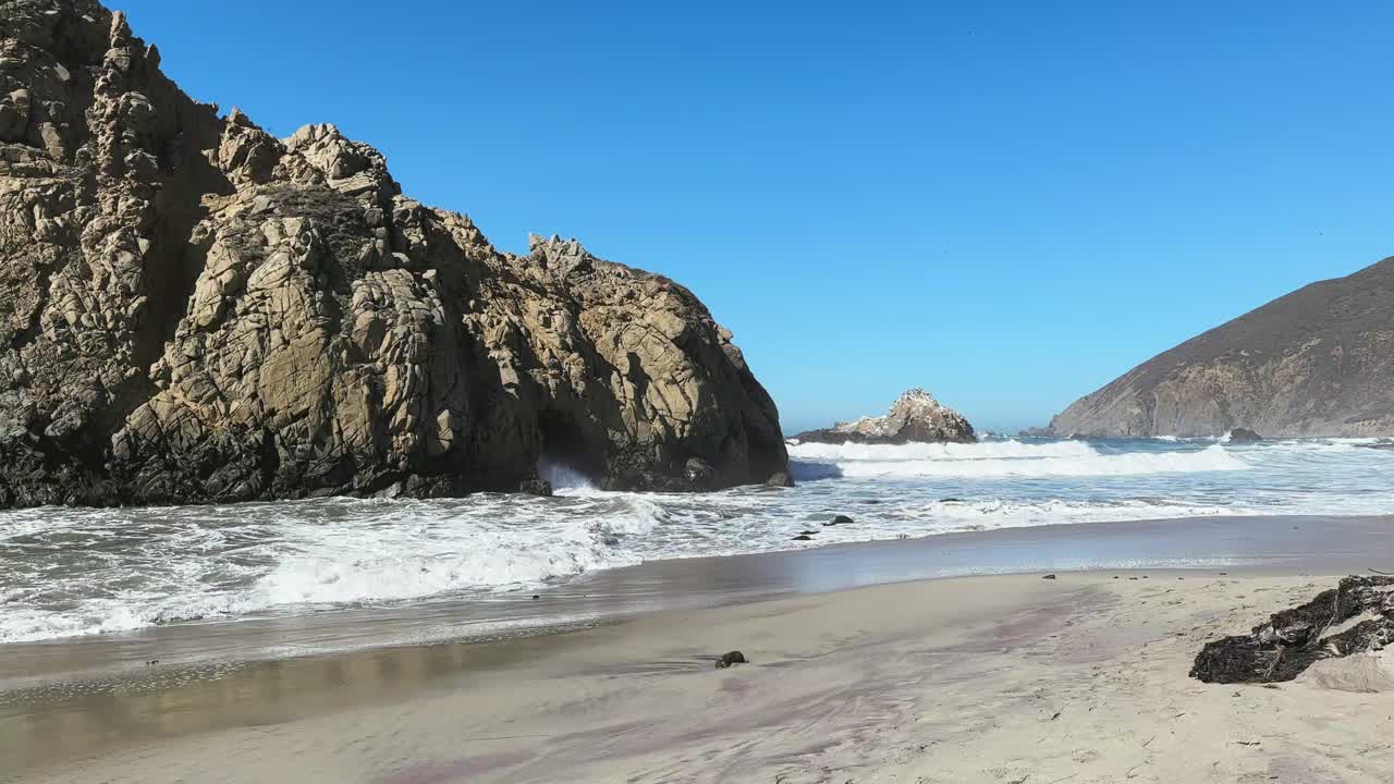 olas, arena y formación de rocas en una playa salvaje